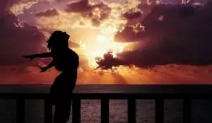 Silhouette einer Person am Geländer mit Sonnenuntergang über dem Meer.