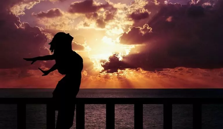 Silhouette einer Person am Geländer mit Sonnenuntergang über dem Meer.